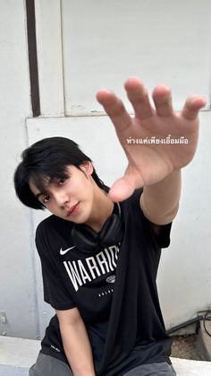 a young man sitting on the ground with his hand up in the air while wearing a black shirt