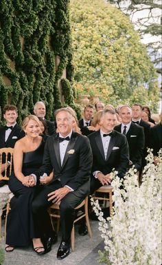 a group of people sitting next to each other in formal wear and tuxedos