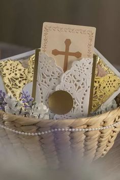 a basket filled with cards and flowers on top of a wooden table next to a cross