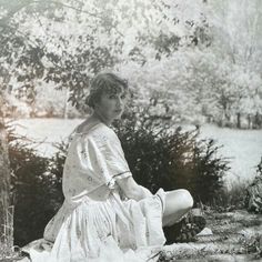 an old black and white photo of a woman sitting on the ground in front of trees