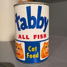 a can of tabby all fish cat food on a table with a spoon next to it