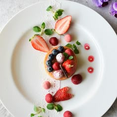 a white plate topped with strawberries and other fruits on top of a table next to flowers