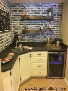 a small kitchen with white cabinets and black counter tops is pictured in this image, there are shelves on the brick wall