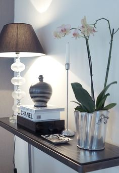 a table with a lamp, vase and books on it next to a flower pot