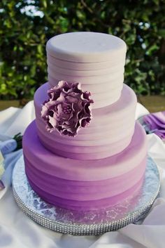 a three tiered cake with purple icing and a flower on the top layer