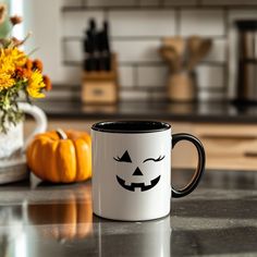 a black and white coffee mug sitting on top of a counter next to a vase with flowers