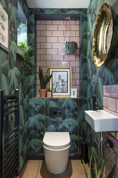 a bathroom with a toilet, sink and plants on the wall next to each other