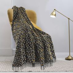 a black and yellow blanket sitting on top of a chair next to a floor lamp