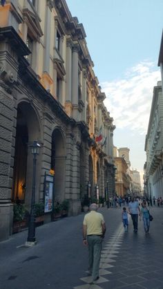 people are walking down the street in front of buildings with arches and pillars on either side