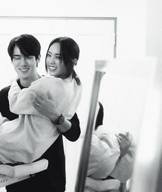 two women are smiling and holding each other in front of a mirror while the woman holds her baby