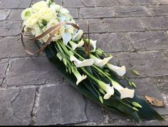 a bouquet of white flowers laying on the ground next to a brick walkway with ribbon tied around it