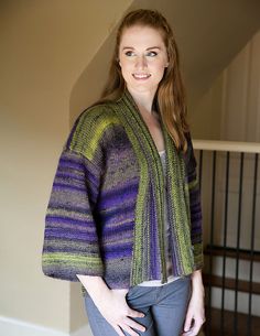 a woman standing in front of a staircase wearing a colorful cardigan sweater and jeans