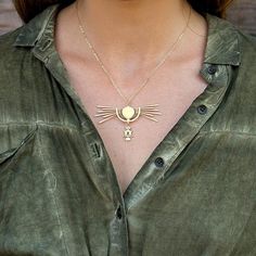 a woman wearing a green shirt with a gold necklace on her neck and an owl charm hanging from the front