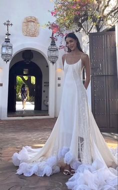 a woman standing in front of a white building wearing a wedding dress with flowers on it