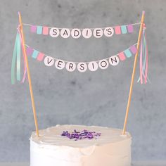 a white cake topped with a pink frosted cake and bunting banner that says sadie's version