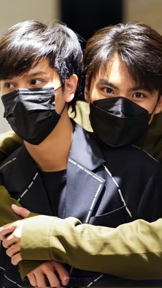 two young men wearing black face masks on their faces, one with his arm around the other's shoulder