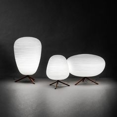 three white lamps sitting next to each other on top of a black surface with wooden legs