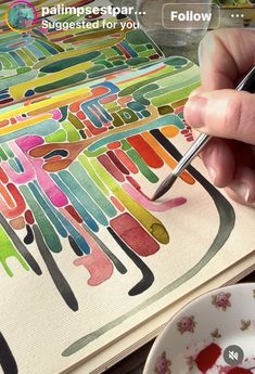 someone is using a pen to paint the letters on a piece of paper with watercolors