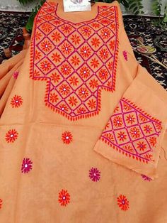 an orange dress with pink and red designs on it sitting on a black table next to flowers