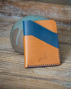 The Timidus card wallet is the perfect choice if you aim at carrying only your daily essentials.  Its fold-over design hints at the curves of the unique Othus twist wallet, yet gives countless colour combination possibilities as well as an extra card slot.  The vertical design of the Timidus also holds your cards more tightly than the horizontal Othus. The Timidus is a 4-slot card wallet. It will hold 6 to 7 cards and some cash from new, while ageing of the leather will allow for another card or two over time.  The Timidus measures 7,5 x 10cm. I only use leather that is 100% vegetable tanned with respect for tradition and our environment. No chemicals are used in the production process, and only left over skins from the food industry are used. This Timidus card wallet is made in a combinat Modern Cognac Wallets With Card Slots, Cognac Card Holder With Rfid Blocking For Everyday Use, Cognac Rfid Blocking Card Holder For Everyday Use, Modern Handmade Brown Card Holder, Modern Handmade Card Holder For Daily Use, Modern Handmade Brown Wallets, Modern Handmade Brown Wallet, Vertical Design, Blue Cross