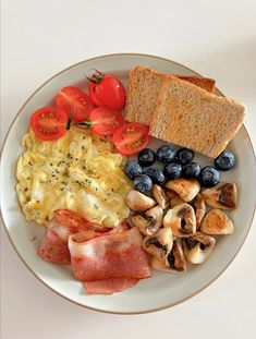 a white plate topped with eggs, bacon, tomatoes and toast next to blueberries