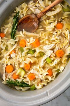 a crock pot filled with chicken noodle soup and a wooden spoon in it