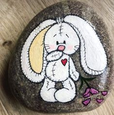 a painted rock with a white bunny holding a pink heart on it's chest