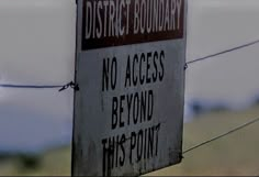 a red and white sign hanging from a barbed wire with the words district boundary no access beyond this point