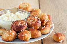 a white plate topped with mini donuts next to a bowl of cream cheese sauce