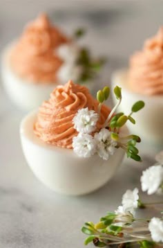 three deviled eggs with orange frosting and white flowers on the top, sitting on a marble surface