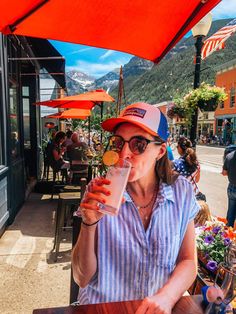 a woman sitting at an outdoor table with a drink in her hand