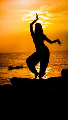 a woman is dancing on the beach at sunset