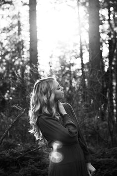 a woman standing in the woods with her hands on her face and looking up at the sky