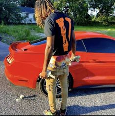 a man standing in front of a red car with dreadlocks on his head