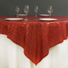 a red table cloth with white plates and wine glasses sitting on top of the table