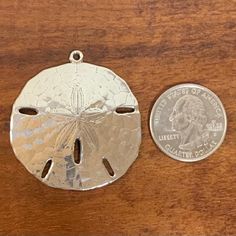 a small silver sand dollar sitting on top of a wooden table next to a coin