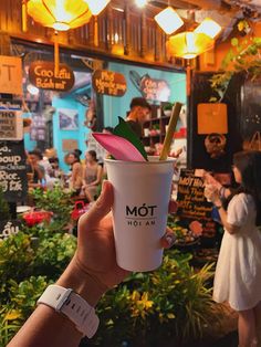 a person holding up a starbucks cup with a flower in it at an outdoor cafe