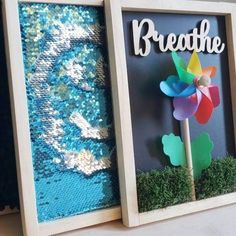 two framed pictures with the words breathe and a pinwheel in them on a shelf