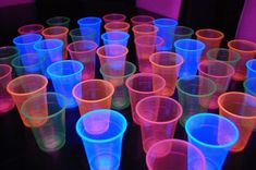 many plastic cups are lined up on a table with colored lights in the dark behind them