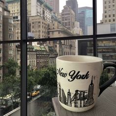 a coffee cup sitting on top of a window sill in front of a cityscape