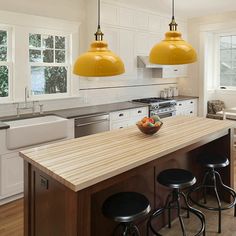 two yellow pendant lights hang over a kitchen island with stools in front of it