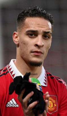 a man holding a soccer ball in his right hand while wearing a red shirt and black gloves