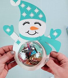 someone holding up a snowman ornament with candy in it's hands