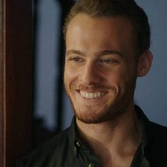 a smiling man in a black shirt and green button up is looking at the camera