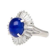 This magnificent ring is crafted from platinum 900 featuring a cathedral style band and gorgeous filigree. Displayed as the center stone is a dazzling cabochon cut star sapphire weighing 7.04 carats, measuring 10.1x8.5mm, captivating with its deep hue and celestial asterism star effect that is well-centered. Surrounding it are 36 brilliant baguette cut diamonds totaling 1.14 carats, adding a shimmering halo to this luxurious piece. This ring is a size 6 and adjustable.  Details: Item Type: Ballerina Ring Metal: Platinum (900 purity) Size: 6 (adjustable) Weight: 9.1 Grams Setting: Cathedral  Center Stone Details: Stone Type: Natural Star Sapphire Carat: 7.04  Cut: Cabochon Color: Blue Measurements: 10.1 x 8.5 mm  Side Stones Details: Type: Natural Diamond Cut: Baguette Carat: 1.14 CTTW  Col Star Effect, Art Ballerina, Ballerina Ring, Sapphire Cocktail Ring, Gold Cocktail Ring, Gold Cocktail, Star Sapphire, Baguette Cut Diamond, Garnet Rings