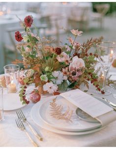 the table is set with white plates and silverware, floral centerpieces, and candles