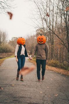 two people walking down a road with pumpkins on their heads and one person holding hands