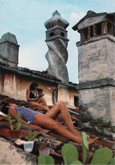 two women sitting on the roof of an old building with chimneys in the back ground