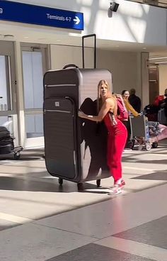 a woman in red is leaning against a luggage bag at an airport with people waiting behind her