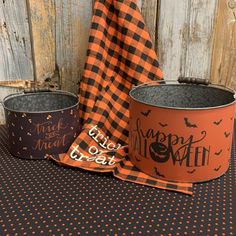 two halloween buckets sitting on top of a black and orange tablecloth next to a wooden fence